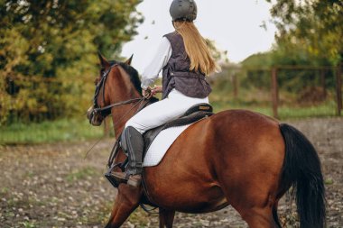 Genç ve güzel bir kadın jokey bir gösteri atlama yarışmasına hazırlanıyor. Bir kadın binici kahverengi bir yarış atı sürüyor. Kadın jokey ata biniyor.