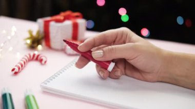 Bir kadın keçeli kalemle kâğıdı uzattığında ne yazacağını düşünür. Noel arkaplanında. Yeni yıl konsepti, planlar ve dilekler..