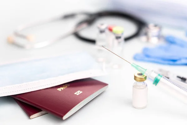 Passports with medical mask with ampoule mock-up for vaccination with syringe on blurred background of doctors office, vaccine concept, compulsory vaccinations for travel.