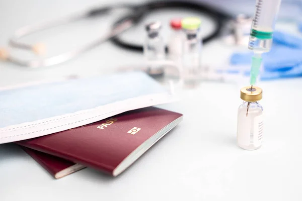 Aşı için ampullü tıbbi maskeli pasaportlar doktor ofisinin bulanık arka planında şırınga, aşı konsepti, seyahat için zorunlu aşılar.