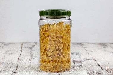 Plastik kaplarda farklı türde makarna. Beyaz desenli arka planda kavanozlarda çeşitli makarna tipleri var. Mutfak dahili fikirleri. Çevre dostu mutfak, sıfır atık ev konsepti.