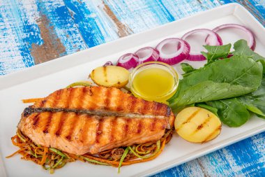 Lezzetli pişmiş somon balığı filetosu. Bir parça fırında somon ızgara limon ve tuzlu beyaz tabakta marul yaprağı. tahta arkaplan.