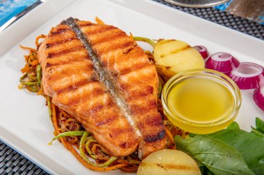 Lezzetli pişmiş somon balığı filetosu. Bir parça fırında somon ızgara limon ve tuzlu beyaz tabakta marul yaprağı. tahta arkaplan.