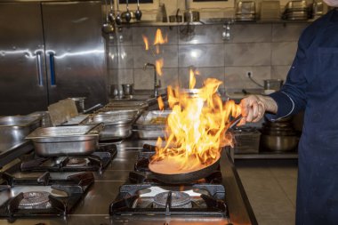 Alevler içinde. Profesyonel Şef, restoranın mutfağında yemek için alev topu yapıyor. Aşçı ocakta tavayla yemek pişiriyor.. 