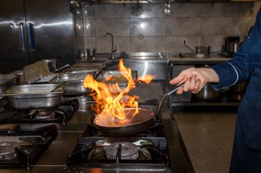 Alevler içinde. Profesyonel Şef, restoranın mutfağında yemek için alev topu yapıyor. Aşçı ocakta tavayla yemek pişiriyor.. 