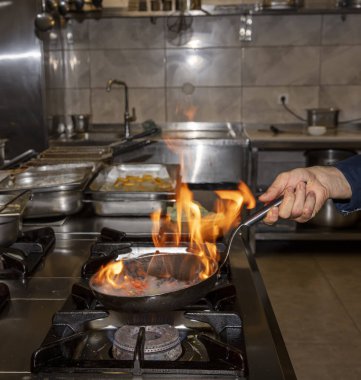 Alevler içinde. Profesyonel Şef, restoranın mutfağında yemek için alev topu yapıyor. Aşçı ocakta tavayla yemek pişiriyor.. 