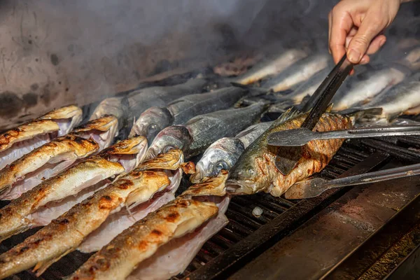 Grilled sea bass fish closeup. In process. European sea-bass, chef is grilling in the kitchen - BBQ