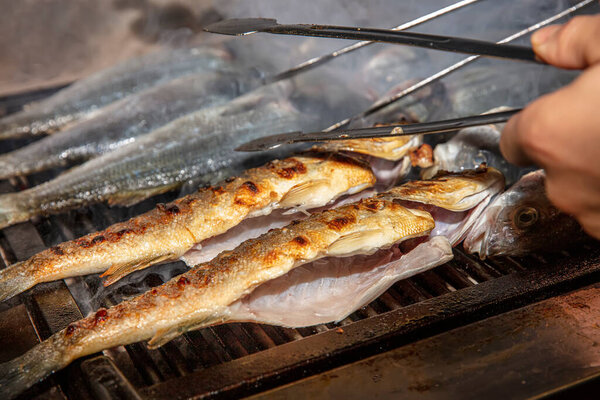 Grilled sea bass fish closeup. In process. European sea-bass, chef is grilling in the kitchen - BBQ