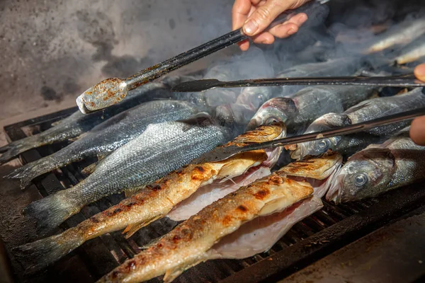 Grilled sea bass fish closeup. In process. European sea-bass, chef is grilling in the kitchen - BBQ