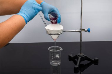 Laboratuvarda filtre kağıdı. Bilimadamları cam hunideki filtre kağıdından filtreleyerek kimyasal filtreleme yapıyorlar. Laboratuvarda eczacı filtreleme maddesi var..
