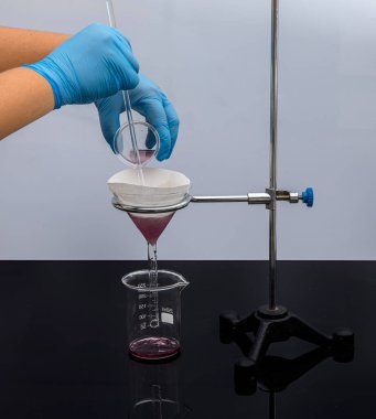 Laboratuvarda filtre kağıdı. Bilimadamları cam hunideki filtre kağıdından filtreleyerek kimyasal filtreleme yapıyorlar. Laboratuvarda eczacı filtreleme maddesi var..