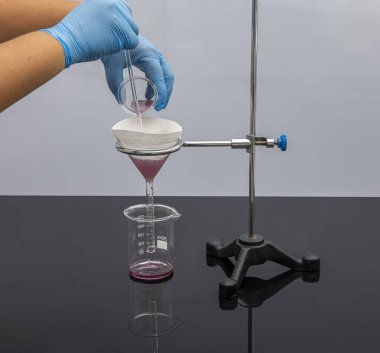 Laboratuvarda filtre kağıdı. Bilimadamları cam hunideki filtre kağıdından filtreleyerek kimyasal filtreleme yapıyorlar. Laboratuvarda eczacı filtreleme maddesi var..