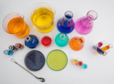 Beyaz masanın üzerinde farklı renkte sıvılar bulunan laboratuvar camları. Beyaz arkaplan üzerinde Ses Ölçümü Laboratuvarı camları.