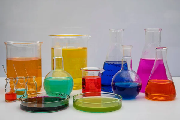 白いテーブルの上に異なる色の液体と研究室のガラス製品 白い背景にボリュームのある研究室用ガラス製品 — ストック写真