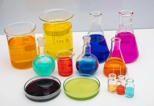 白いテーブルの上に異なる色の液体と研究室のガラス製品 白い背景にボリュームのある研究室用ガラス製品 — ストック写真