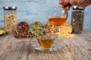 Kaba ahşap arka planda, adaçayı ve bal tazeleyici. Seçili odak. Nane yaprakları, kaşıklı bal ve bir fincan sıcak çay. Bitkisellik ve modern eczacılık kavramı.