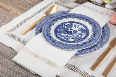 Boş sofra takımı, seramik tabak, baharat kâseleri, bıçak, eski bir ahşap masanın üzerinde eski keten kumaştan yapılmış çatal. Kır mavisi tarzı. Üst görünüm.