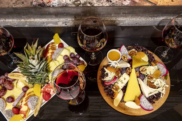 Cheese and fruit plate on the table by the fireplace. A sumptuous feast of fresh fruits and veggies, rustic breads, cheese and wine in the glass on a table in a rustic setting.