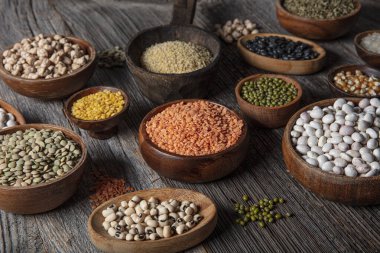 Vegan protein source.Various assortment of legumes, lentils, chickpea and beans assortment in different bowls on wooden table. Top view.