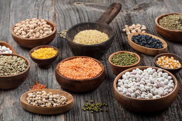 Vegan protein source.Various assortment of legumes, lentils, chickpea and beans assortment in different bowls on wooden table. Top view.
