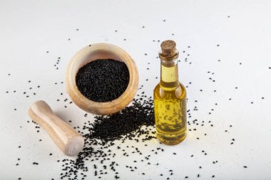 Kasede siyah kimyon tohumları ve cam şişede gerekli yağ. Beyaz arkaplanda Nigella sativa izole. 