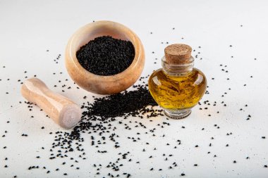 Kasede siyah kimyon tohumları ve cam şişede gerekli yağ. Beyaz arkaplanda Nigella sativa izole. 
