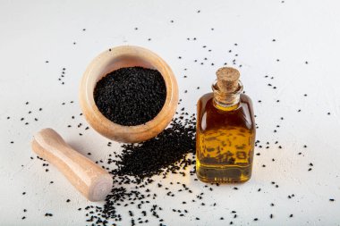 Kasede siyah kimyon tohumları ve cam şişede gerekli yağ. Beyaz arkaplanda Nigella sativa izole. 