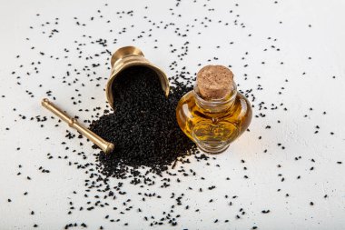 Kasede siyah kimyon tohumları ve cam şişede gerekli yağ. Beyaz arkaplanda Nigella sativa izole. 
