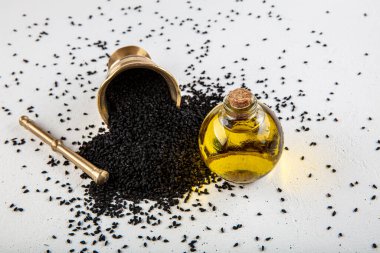 Kasede siyah kimyon tohumları ve cam şişede gerekli yağ. Beyaz arkaplanda Nigella sativa izole. 