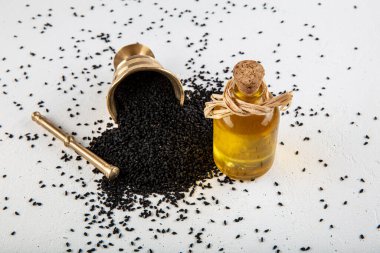 Kasede siyah kimyon tohumları ve cam şişede gerekli yağ. Beyaz arkaplanda Nigella sativa izole. 