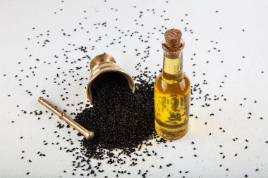 Kasede siyah kimyon tohumları ve cam şişede gerekli yağ. Beyaz arkaplanda Nigella sativa izole. 
