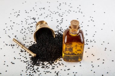 Kasede siyah kimyon tohumları ve cam şişede gerekli yağ. Beyaz arkaplanda Nigella sativa izole. 