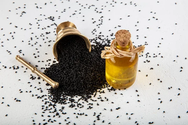 Kasede siyah kimyon tohumları ve cam şişede gerekli yağ. Beyaz arkaplanda Nigella sativa izole. 