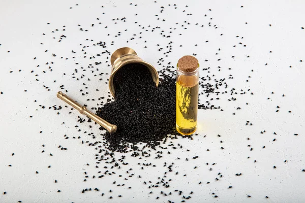 Kasede siyah kimyon tohumları ve cam şişede gerekli yağ. Beyaz arkaplanda Nigella sativa izole. 