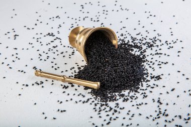 Nigella sativa tohumları ayrıca siyah kimyon, kalo jeera, kalonji ve siyah karanfil olarak da bilinir demir kepçesinde ve beyaz ahşap zemin üzerinde havan ve kopyalama alanı ile birlikte.