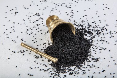 Nigella sativa tohumları ayrıca siyah kimyon, kalo jeera, kalonji ve siyah karanfil olarak da bilinir demir kepçesinde ve beyaz ahşap zemin üzerinde havan ve kopyalama alanı ile birlikte.