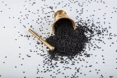 Nigella sativa tohumları ayrıca siyah kimyon, kalo jeera, kalonji ve siyah karanfil olarak da bilinir demir kepçesinde ve beyaz ahşap zemin üzerinde havan ve kopyalama alanı ile birlikte.