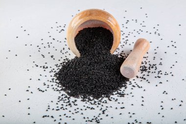 Nigella sativa tohumları ayrıca siyah kimyon, kalo jeera, kalonji ve siyah karanfil olarak da bilinir demir kepçesinde ve beyaz ahşap zemin üzerinde havan ve kopyalama alanı ile birlikte.