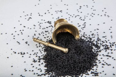 Nigella sativa tohumları ayrıca siyah kimyon, kalo jeera, kalonji ve siyah karanfil olarak da bilinir demir kepçesinde ve beyaz ahşap zemin üzerinde havan ve kopyalama alanı ile birlikte.