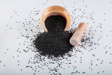 Nigella sativa tohumları ayrıca siyah kimyon, kalo jeera, kalonji ve siyah karanfil olarak da bilinir demir kepçesinde ve beyaz ahşap zemin üzerinde havan ve kopyalama alanı ile birlikte.