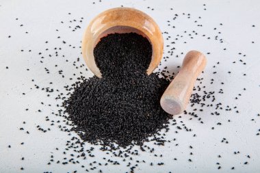 Nigella sativa tohumları ayrıca siyah kimyon, kalo jeera, kalonji ve siyah karanfil olarak da bilinir demir kepçesinde ve beyaz ahşap zemin üzerinde havan ve kopyalama alanı ile birlikte.