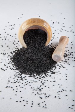 Nigella sativa tohumları ayrıca siyah kimyon, kalo jeera, kalonji ve siyah karanfil olarak da bilinir demir kepçesinde ve beyaz ahşap zemin üzerinde havan ve kopyalama alanı ile birlikte.