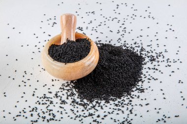 Nigella sativa tohumları ayrıca siyah kimyon, kalo jeera, kalonji ve siyah karanfil olarak da bilinir demir kepçesinde ve beyaz ahşap zemin üzerinde havan ve kopyalama alanı ile birlikte.
