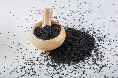 Nigella sativa tohumları ayrıca siyah kimyon, kalo jeera, kalonji ve siyah karanfil olarak da bilinir demir kepçesinde ve beyaz ahşap zemin üzerinde havan ve kopyalama alanı ile birlikte.