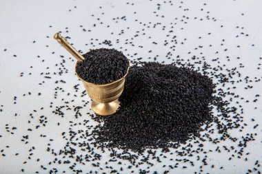 Nigella sativa tohumları ayrıca siyah kimyon, kalo jeera, kalonji ve siyah karanfil olarak da bilinir demir kepçesinde ve beyaz ahşap zemin üzerinde havan ve kopyalama alanı ile birlikte.