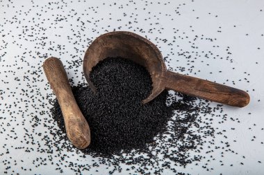 Nigella sativa tohumları ayrıca siyah kimyon, kalo jeera, kalonji ve siyah karanfil olarak da bilinir demir kepçesinde ve beyaz ahşap zemin üzerinde havan ve kopyalama alanı ile birlikte.