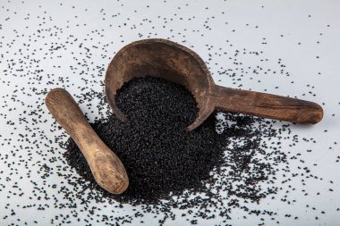 Nigella sativa tohumları ayrıca siyah kimyon, kalo jeera, kalonji ve siyah karanfil olarak da bilinir demir kepçesinde ve beyaz ahşap zemin üzerinde havan ve kopyalama alanı ile birlikte.