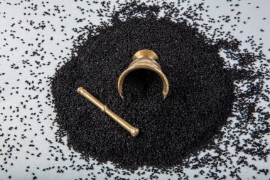 Nigella sativa tohumları ayrıca siyah kimyon, kalo jeera, kalonji ve siyah karanfil olarak da bilinir demir kepçesinde ve beyaz ahşap zemin üzerinde havan ve kopyalama alanı ile birlikte.