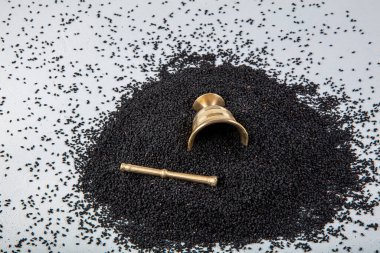 Nigella sativa tohumları ayrıca siyah kimyon, kalo jeera, kalonji ve siyah karanfil olarak da bilinir demir kepçesinde ve beyaz ahşap zemin üzerinde havan ve kopyalama alanı ile birlikte.