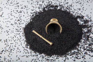 Nigella sativa tohumları ayrıca siyah kimyon, kalo jeera, kalonji ve siyah karanfil olarak da bilinir demir kepçesinde ve beyaz ahşap zemin üzerinde havan ve kopyalama alanı ile birlikte.